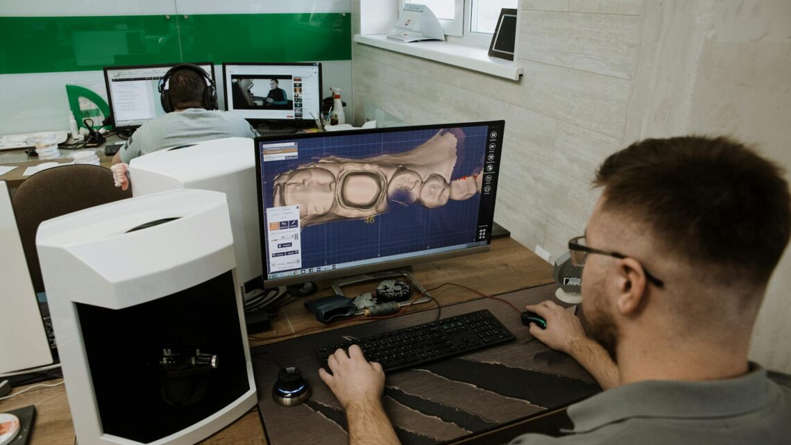 Back view of anonymous male programmer sitting at table and creating 3d model of teeth while working in modern dental laboratory