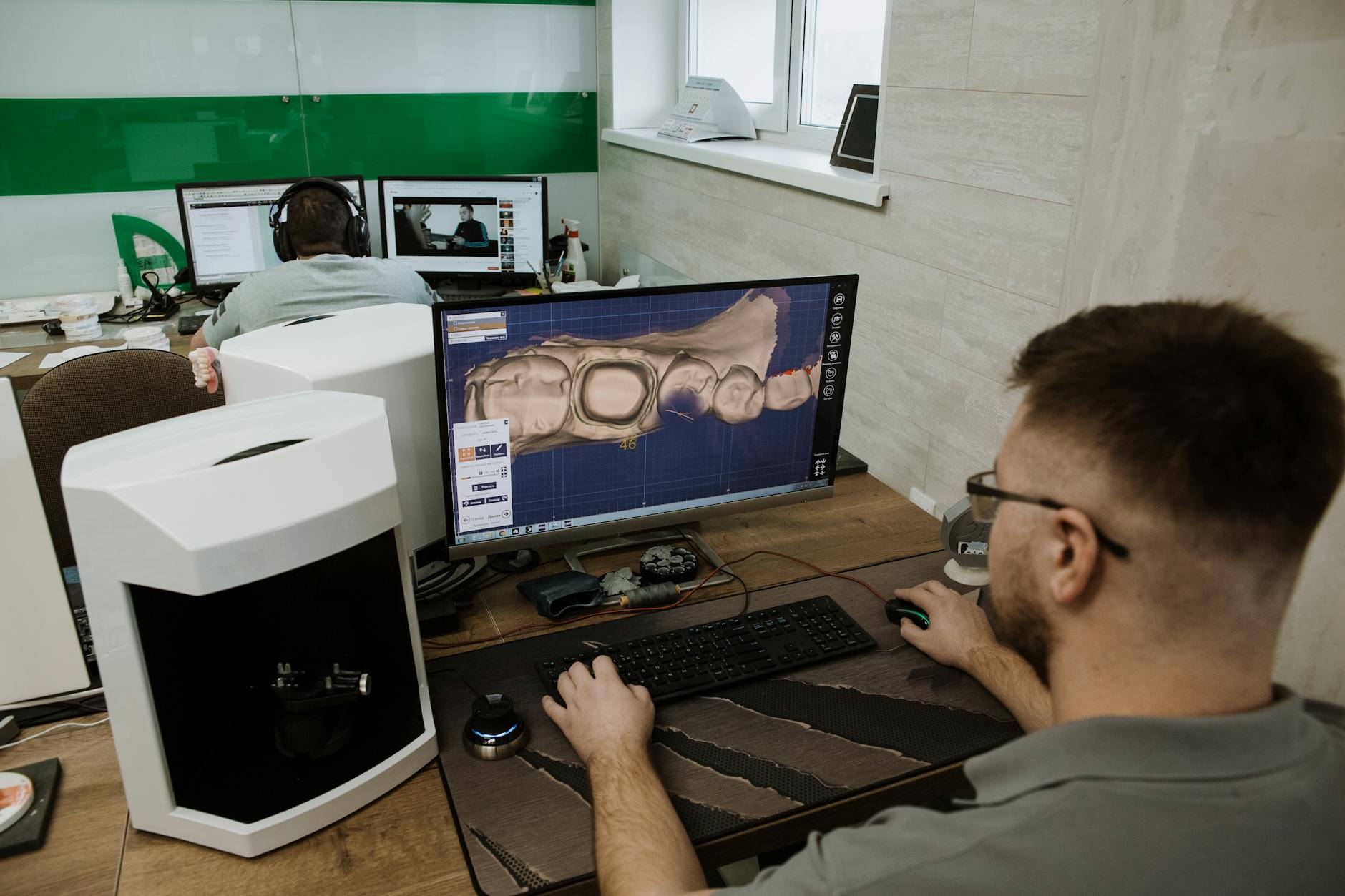 Back view of anonymous male programmer sitting at table and creating 3d model of teeth while working in modern dental laboratory
