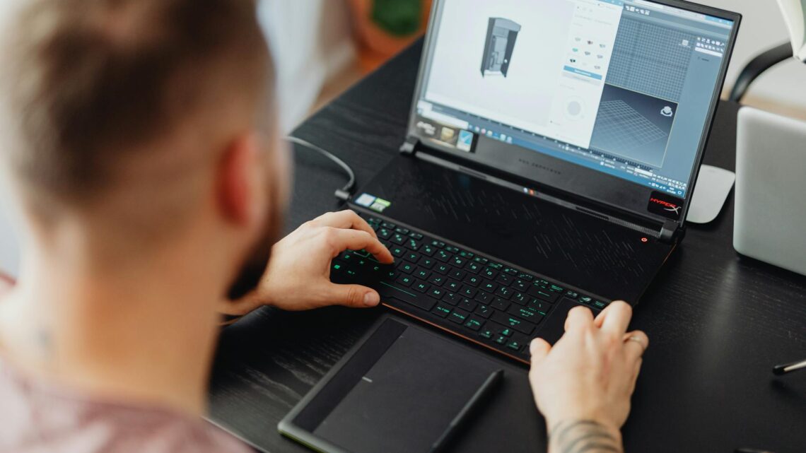 Man using laptop and tablet for 3D design, showcasing modern digital work environment.