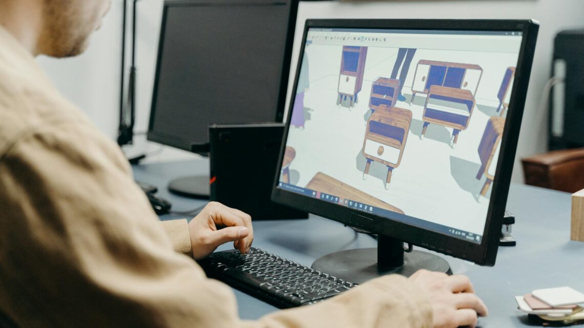 A product designer using a computer for 3D furniture modeling in an office setting.