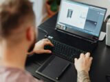 Man using laptop and tablet for 3D design, showcasing modern digital work environment.