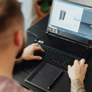 Man using laptop and tablet for 3D design, showcasing modern digital work environment.