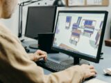 A product designer using a computer for 3D furniture modeling in an office setting.