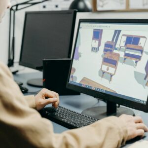 A product designer using a computer for 3D furniture modeling in an office setting.