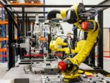 Close-up of a yellow industrial robotic arm in action at a modern manufacturing facility.