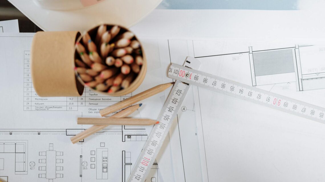 Colorful pencils and ruler atop architectural blueprints on a workspace.