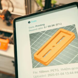 Close-up of a digital tablet displaying a 3D printing process in a workshop setting.