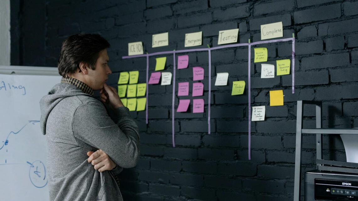 Adult male focusing on task planning using sticky notes on a black wall in a contemporary office setting.