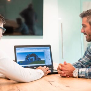 Two professionals discussing a 3D architectural design on a laptop in a modern office.