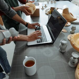 Hands on laptop in a creative workspace with 3D models and prototypes.