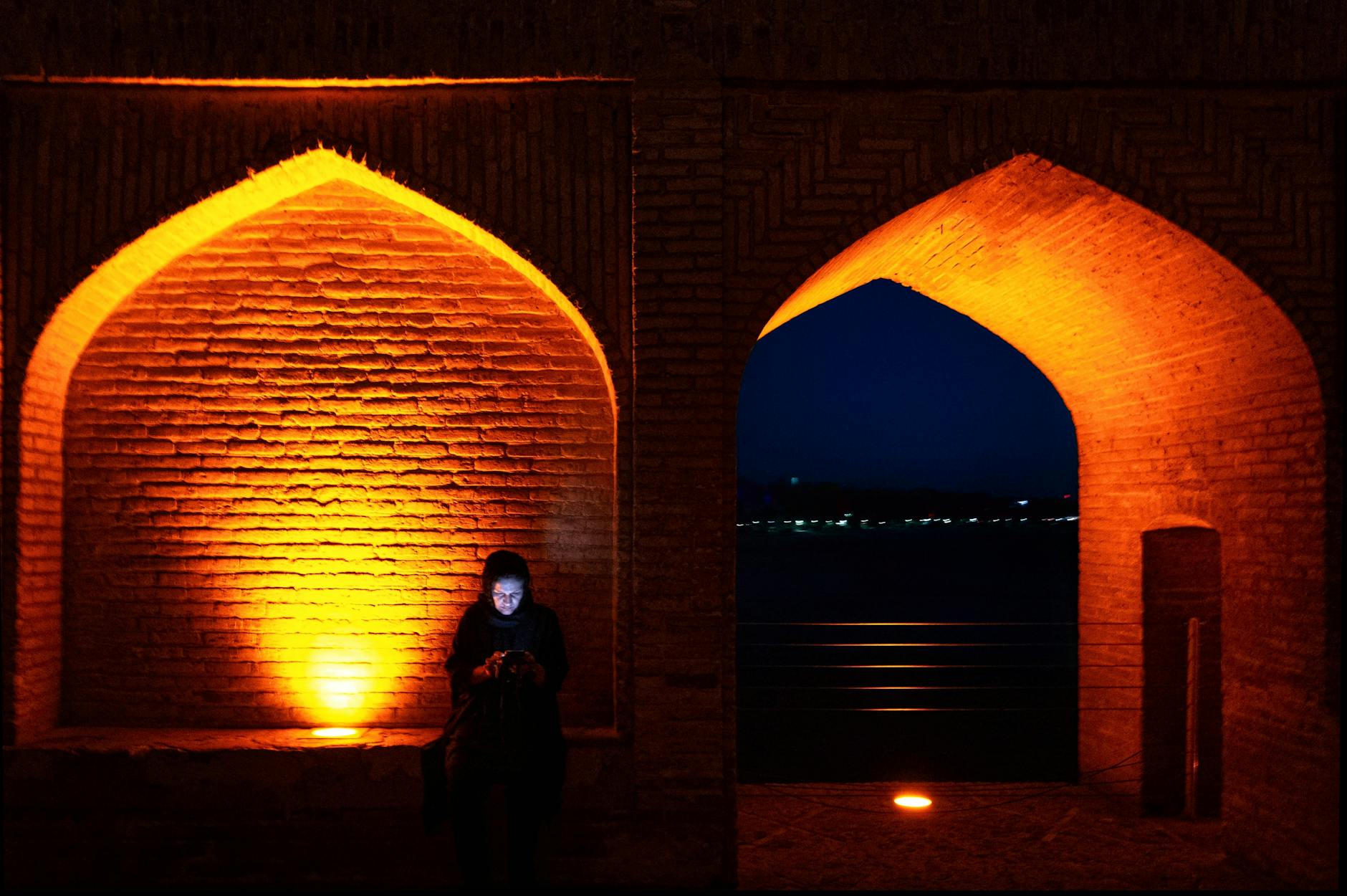 A solitary woman illuminated by city lights at Si-o-se-pol Bridge, Isfahan.