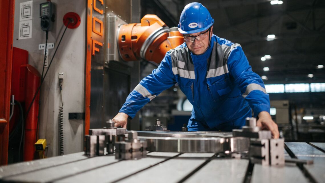 Male worker in blue uniform operates machinery in an industrial factory setting, showcasing engineering and industry.