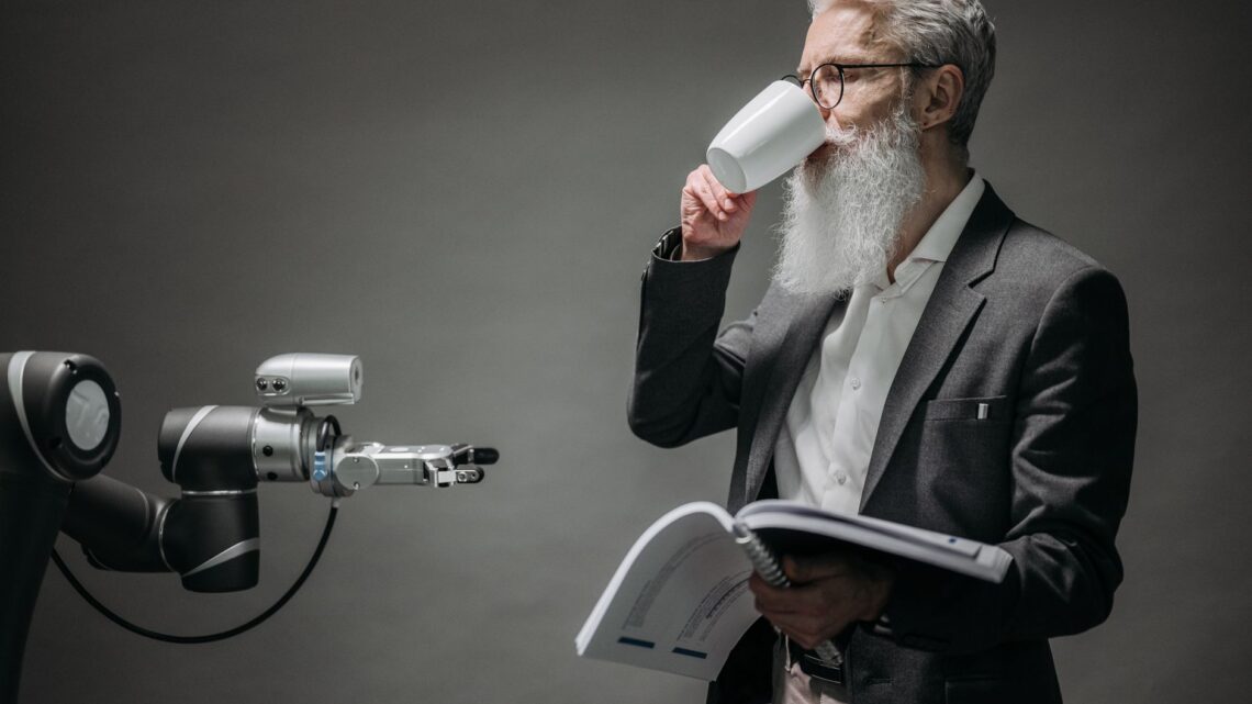A senior man interacts with a robot while holding a book, symbolizing technology and innovation.