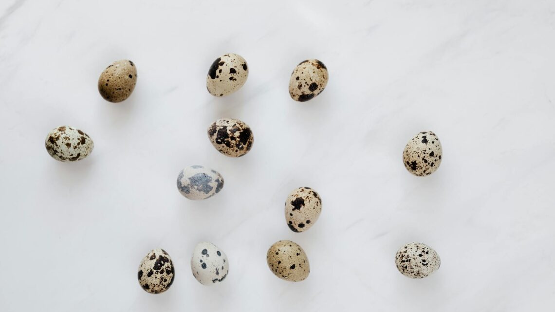 Top view of natural quail eggs placed chaotically on white table during cooking process in kitchen