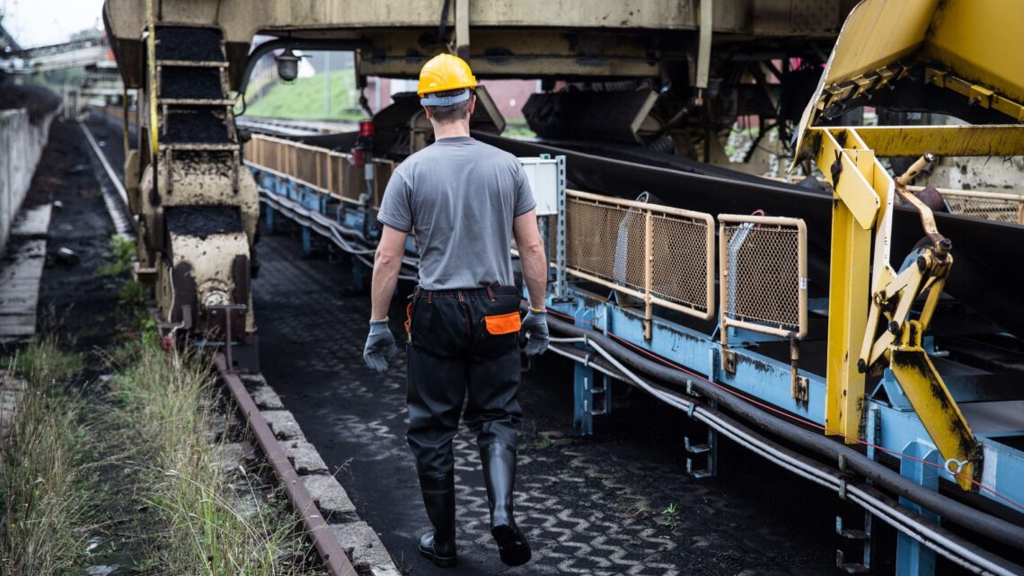 A worker in safety gear examines industrial machinery in an outdoor setting, showcasing industry work.
