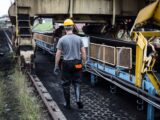 A worker in safety gear examines industrial machinery in an outdoor setting, showcasing industry work.