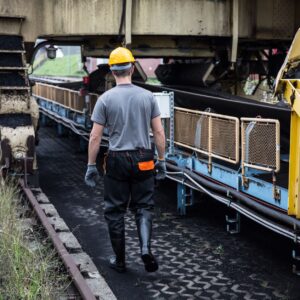A worker in safety gear examines industrial machinery in an outdoor setting, showcasing industry work.