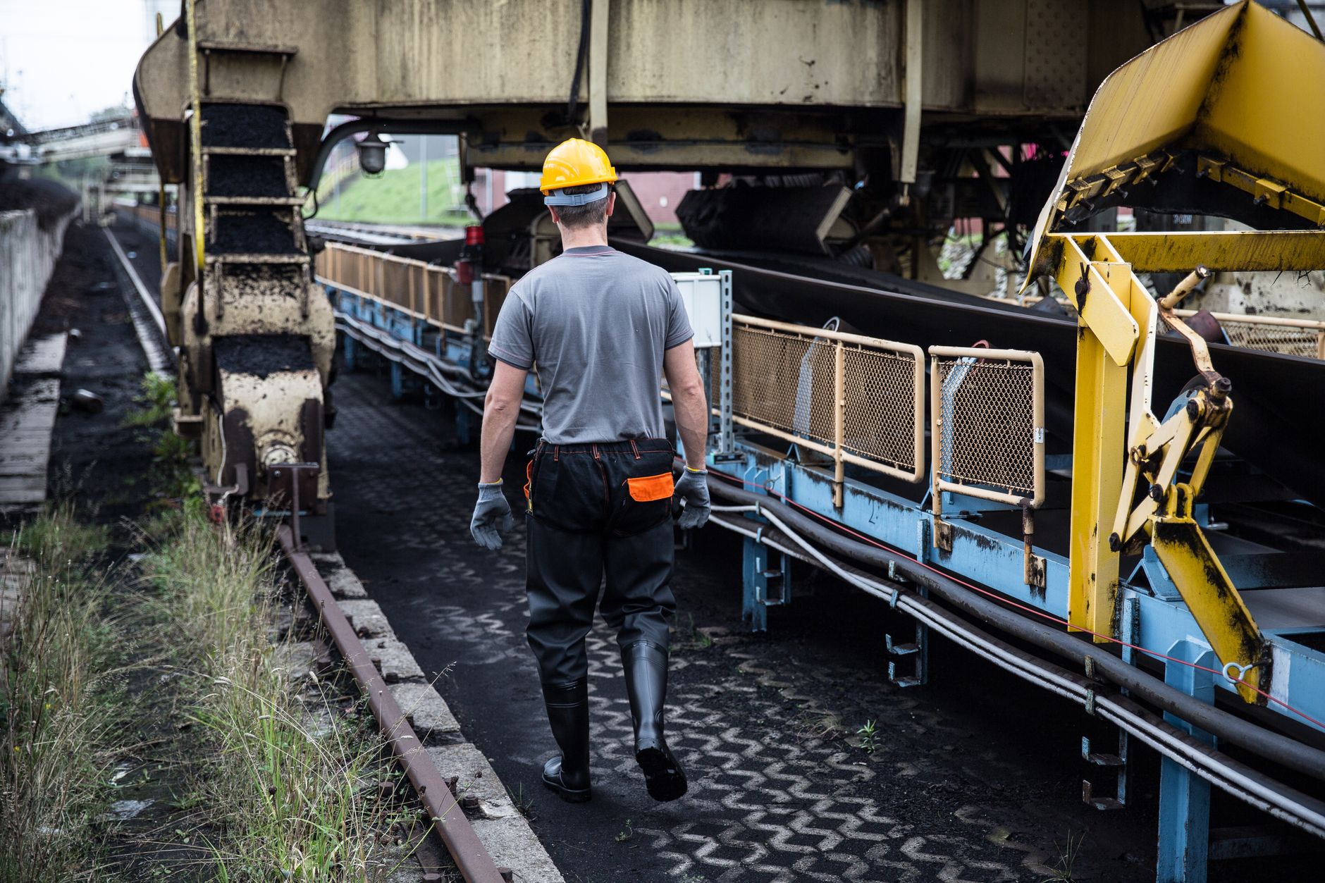 A worker in safety gear examines industrial machinery in an outdoor setting, showcasing industry work.