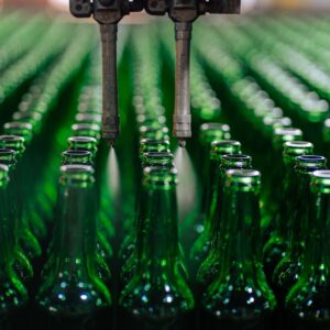 Rows of green glass bottles on an automated production line in a factory setting.