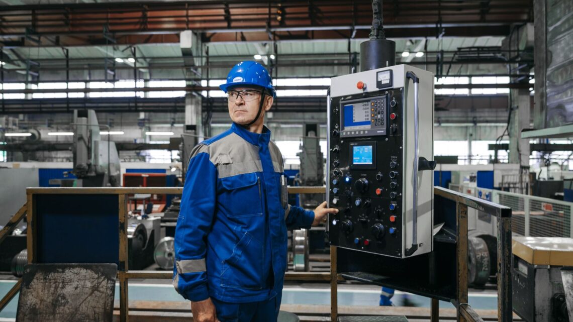 Male factory worker in protective gear operates machinery indoors.