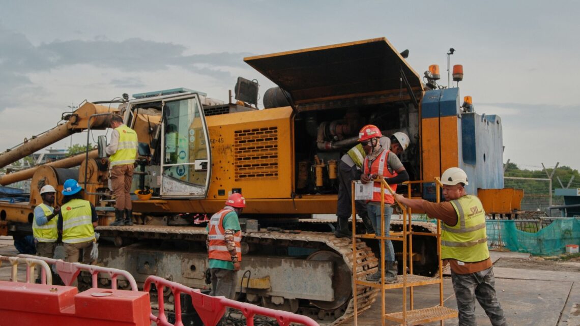 Group of construction workers handling machinery at a worksite with safety gear.