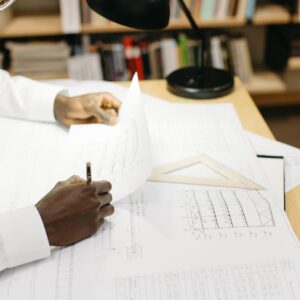 Black male architect working on blueprints at a desk in a well-lit office.