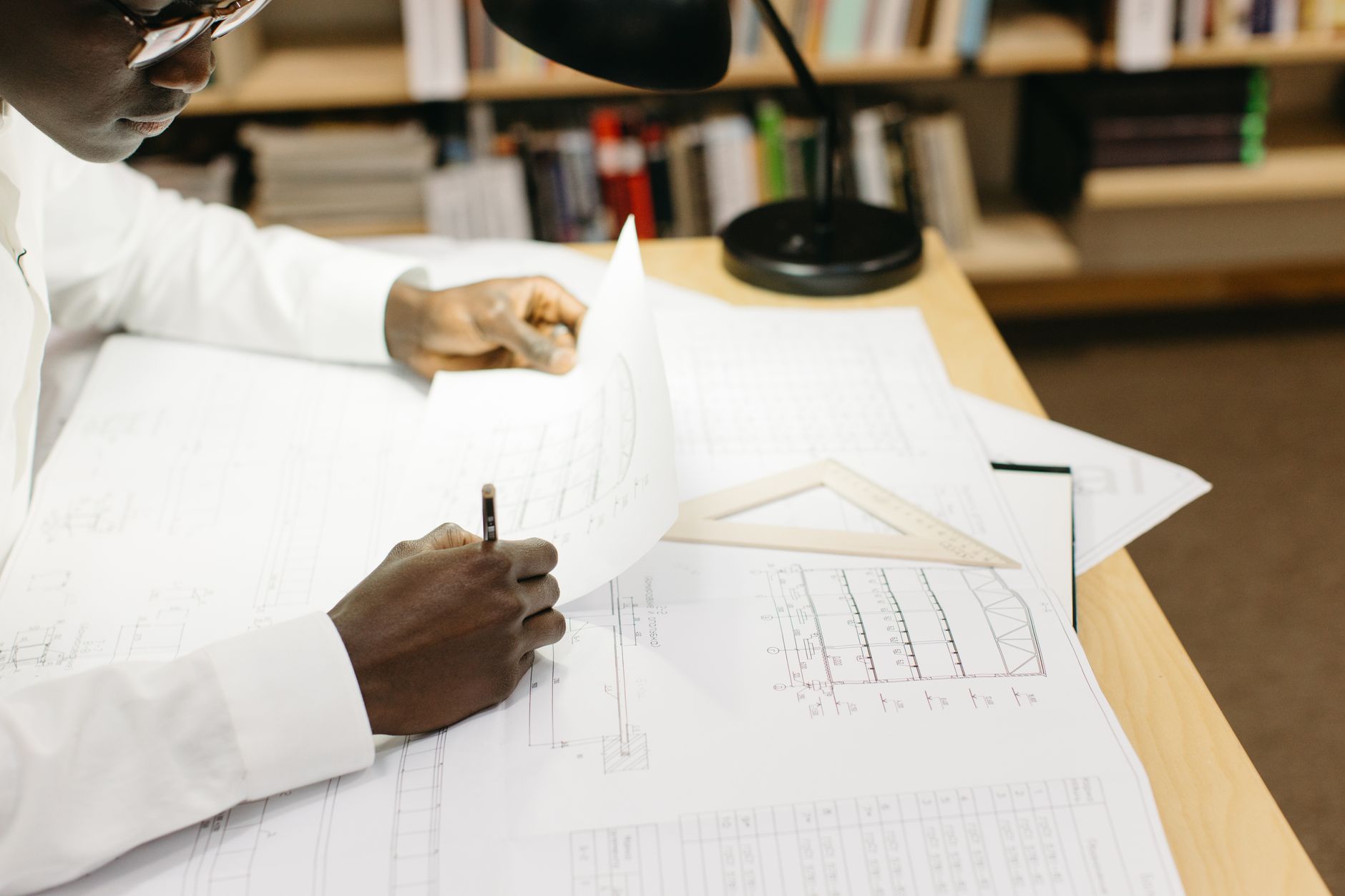 Black male architect working on blueprints at a desk in a well-lit office.
