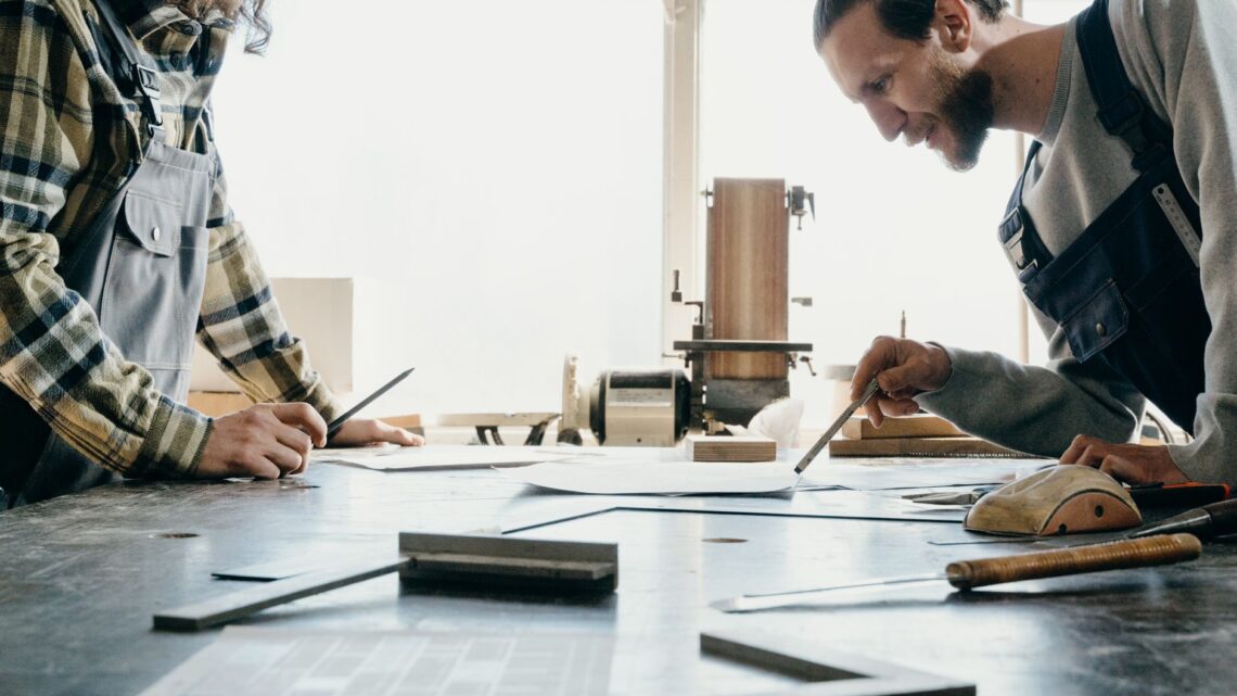 Two craftsmen working on a project in a sunlit workshop. Collaborative effort.