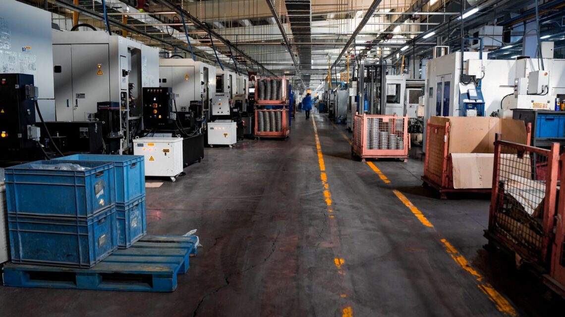Vast industrial factory floor with machinery, crates, and structured workstations.
