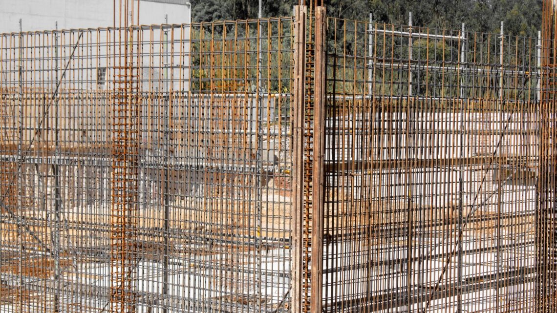 Close-up view of rusting reinforcement steel bars at a construction site with surrounding wooden formwork.