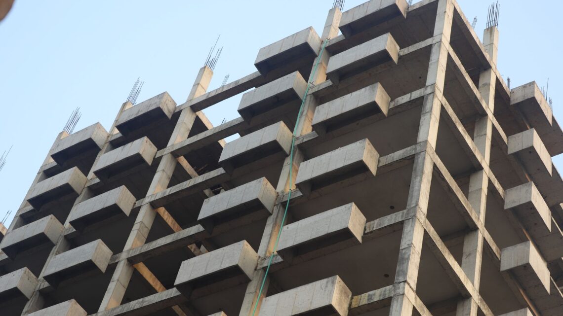 A concrete building skeleton under construction with visible beams and sky backdrop.