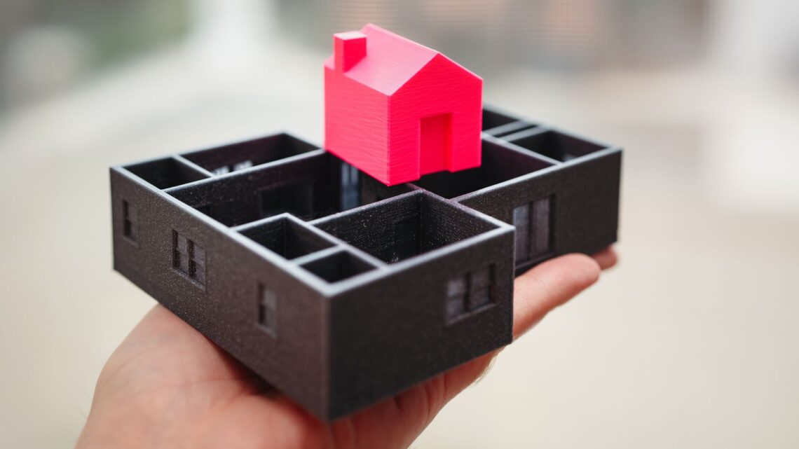 A hand holding a 3D printed model of a house and floor plan, showcasing architectural design.