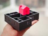 A hand holding a 3D printed model of a house and floor plan, showcasing architectural design.