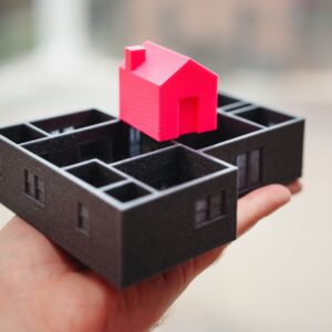 A hand holding a 3D printed model of a house and floor plan, showcasing architectural design.