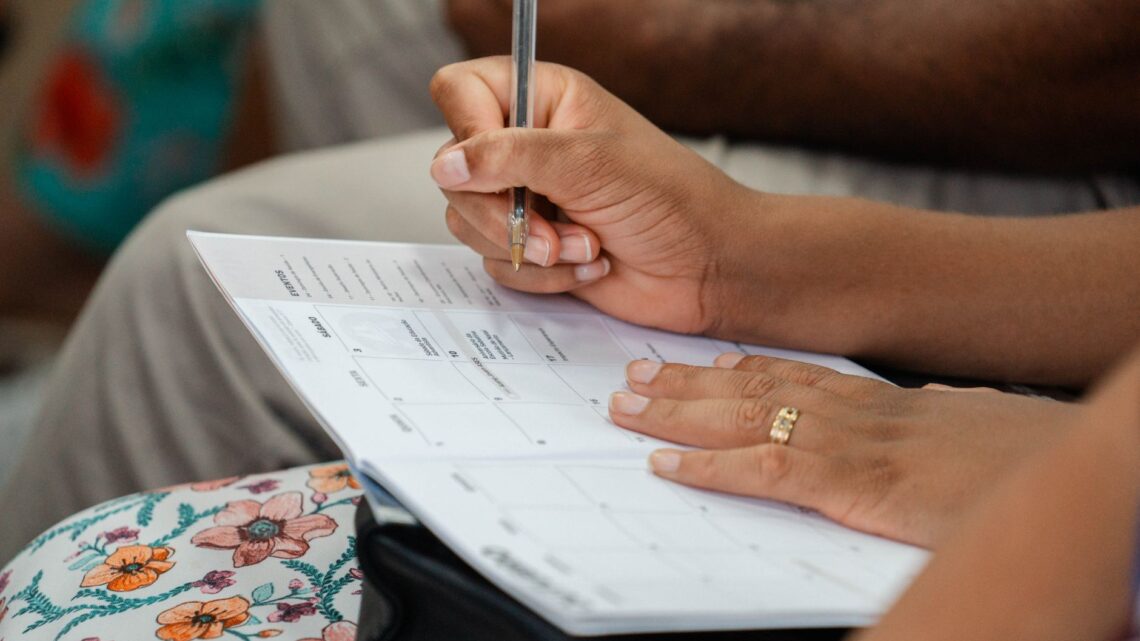 A woman writing in a calendar planner, highlighting organization and time management.