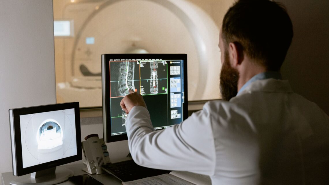 Medical professional reviewing MRI scans on computer screens for diagnostic purposes.
