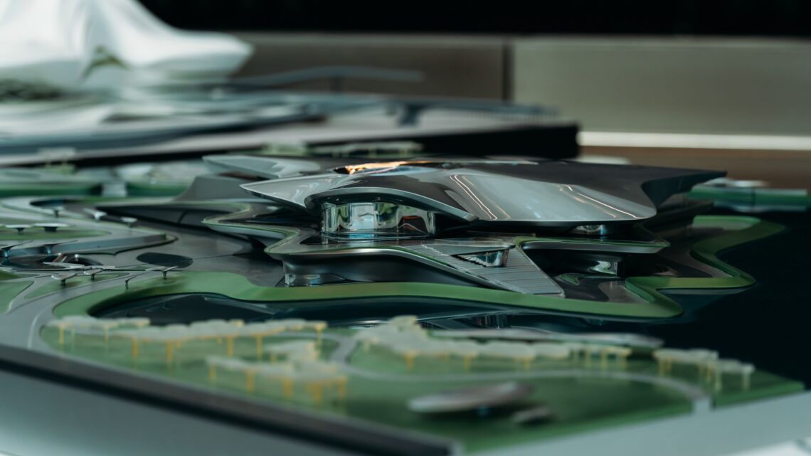 A sleek, futuristic architectural model featuring a metallic design with surrounding green landscape.