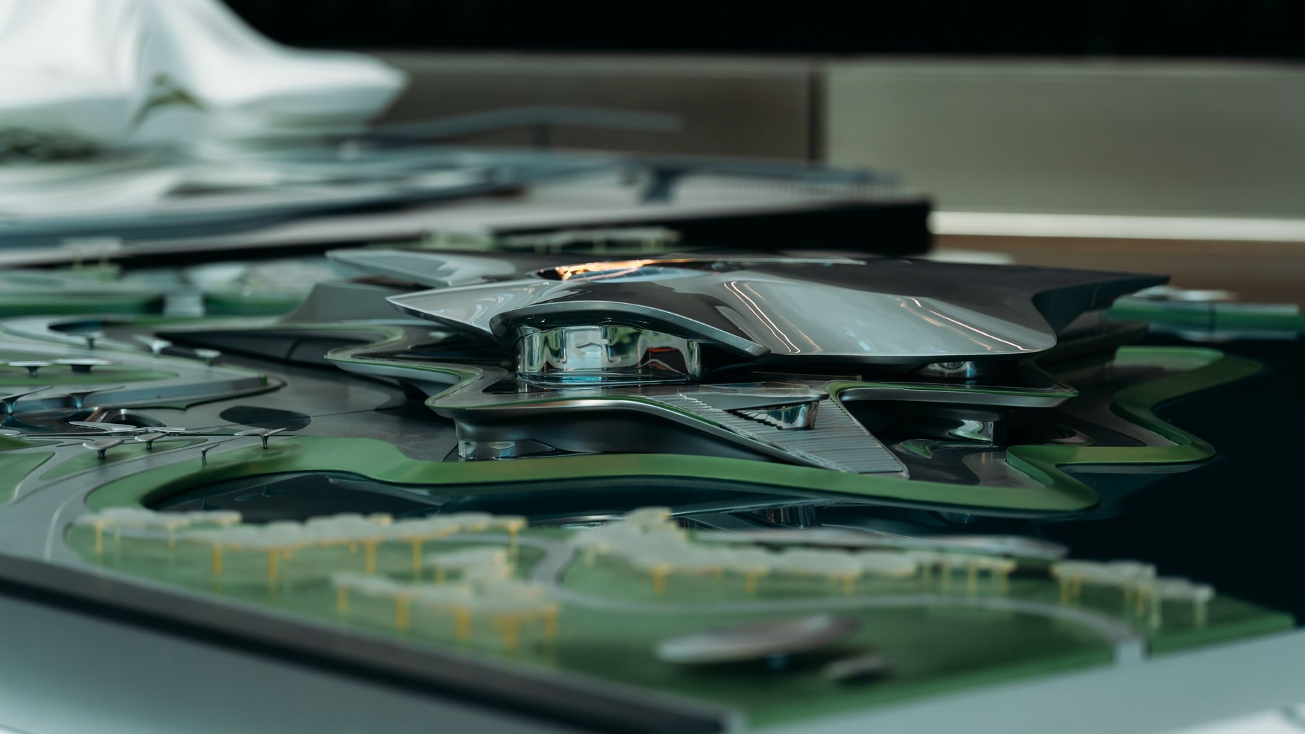 A sleek, futuristic architectural model featuring a metallic design with surrounding green landscape.