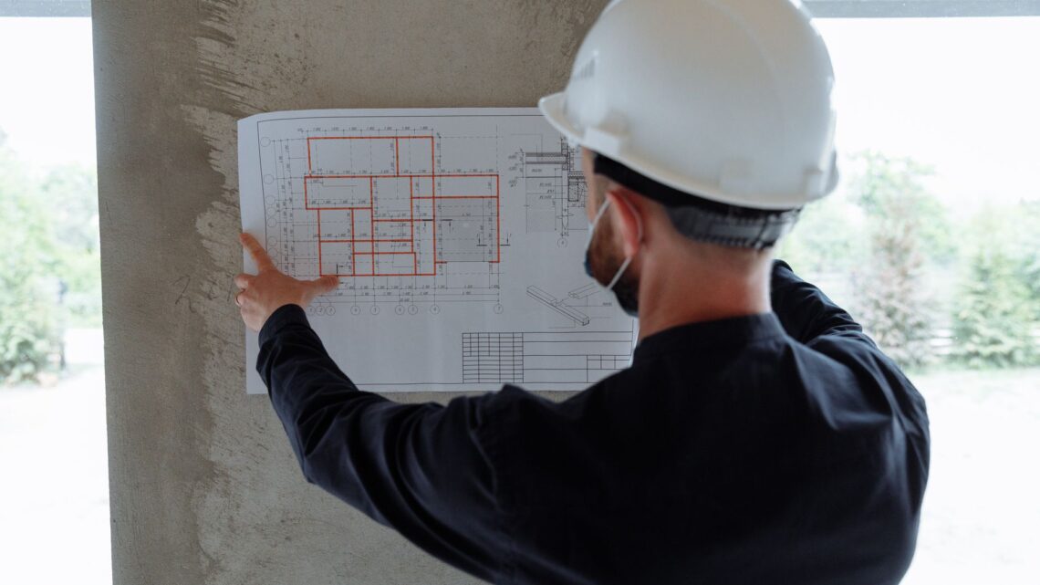 Engineer in hardhat reviewing architectural floor plans at construction site.