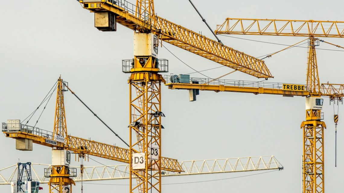 Cluster of yellow tower cranes at a construction site with a gloomy sky background.