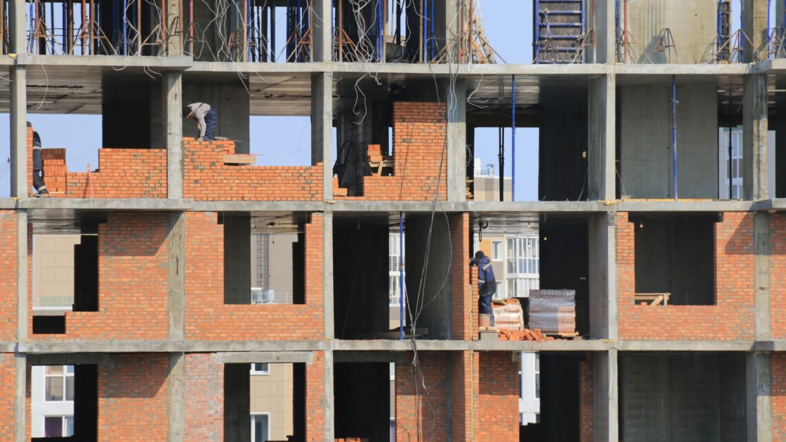 Workers engaged in bricklaying on a multi-story building under construction in an urban area.