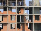 Workers engaged in bricklaying on a multi-story building under construction in an urban area.