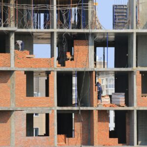 Workers engaged in bricklaying on a multi-story building under construction in an urban area.