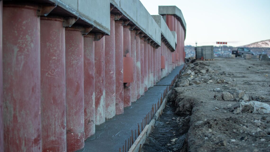 View of a construction site featuring large concrete columns, earthwork, and machinery.