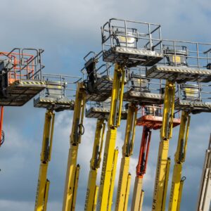 Multiple aerial work platforms with colorful booms reaching skyward against a cloud-dotted backdrop.