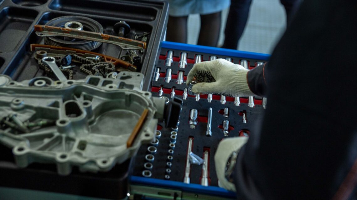 A mechanic in gloves organizing engine parts and tools in a workshop setting.