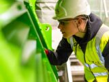 Safety-conscious factory worker inspects machinery for quality control in industrial setting.