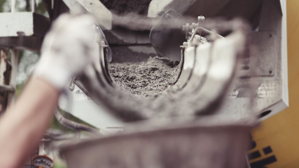 Close-up of concrete being poured from a mixer truck at a construction site with a worker's hand visible.