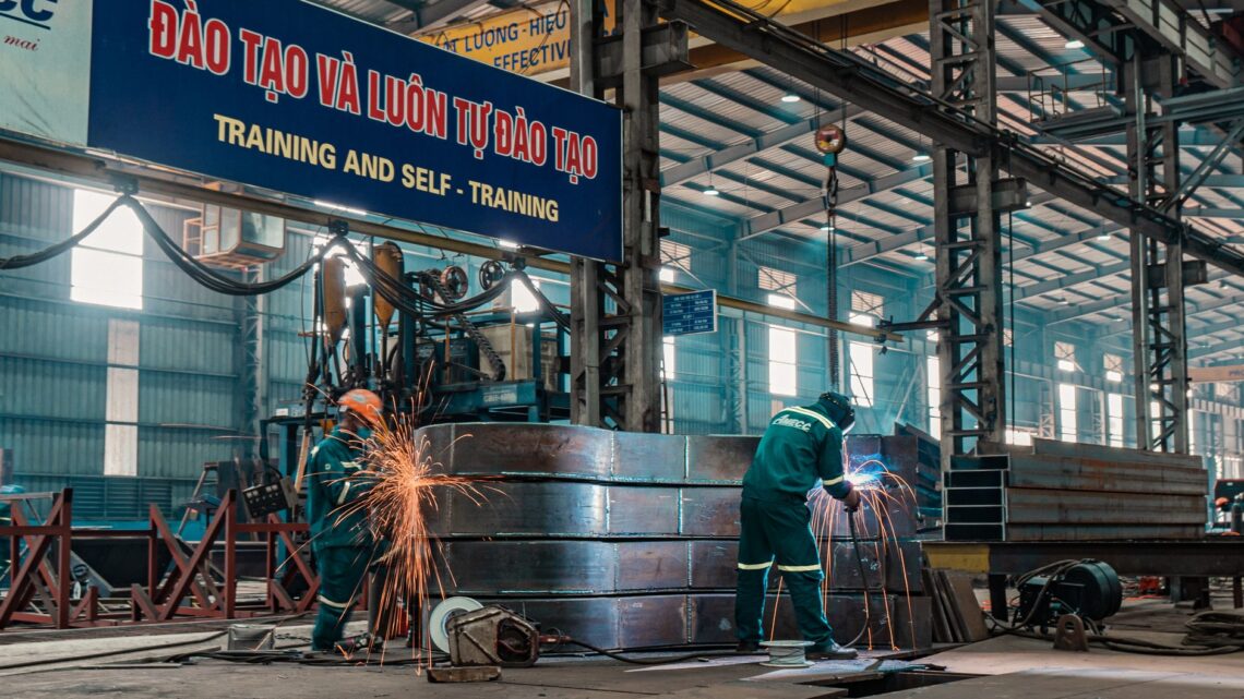 Workers weld metal structures in a bustling industrial factory, showcasing a dynamic work environment.