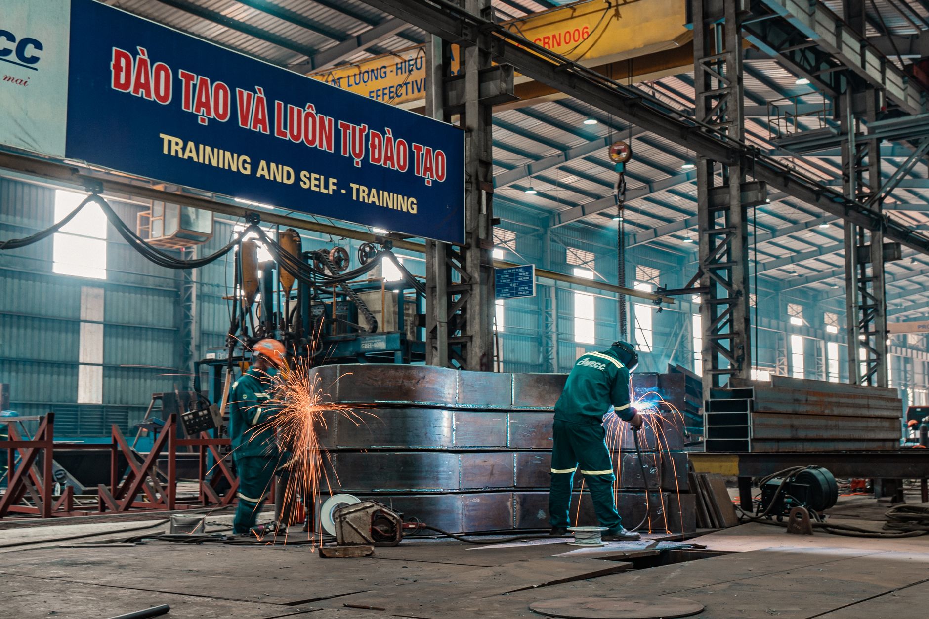 Workers weld metal structures in a bustling industrial factory, showcasing a dynamic work environment.